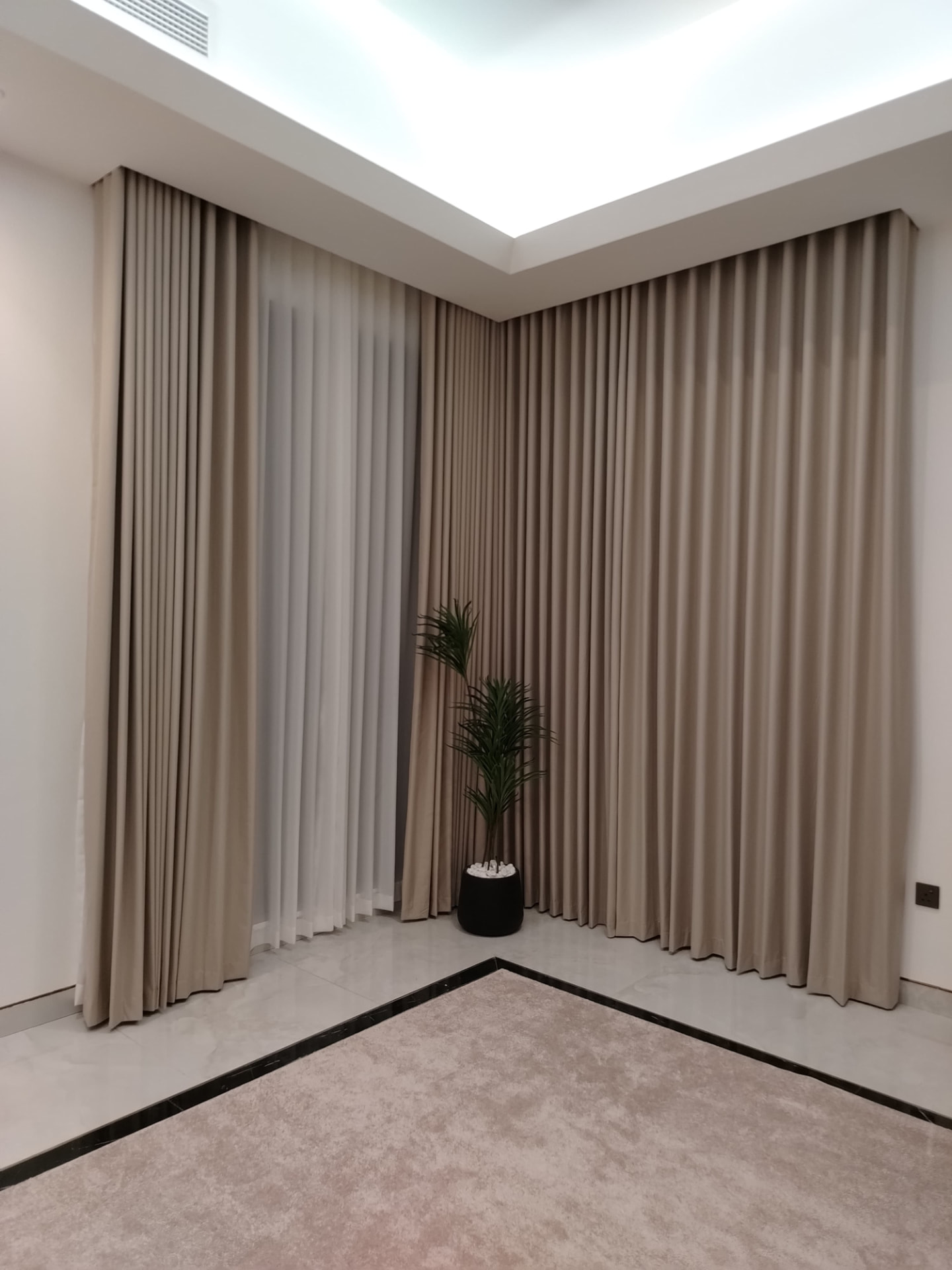 Beige wave curtains wrapping a corner window with sheers behind